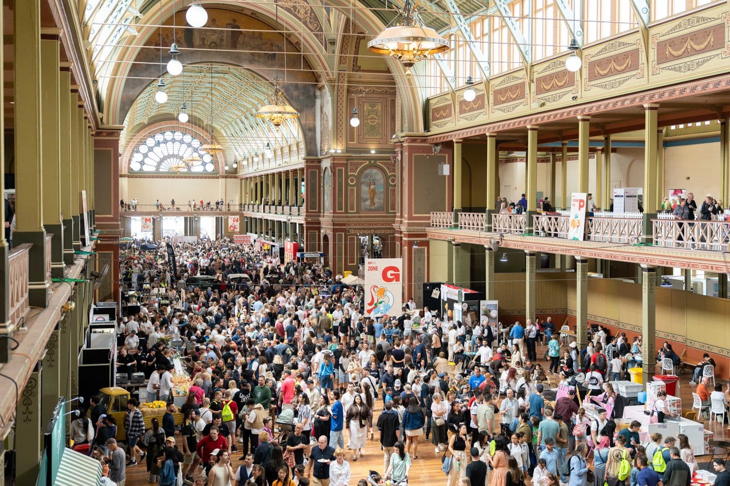 Crowded interior of heritage building with ornate ceiling, grand arches, multiple levels, and festival crowd