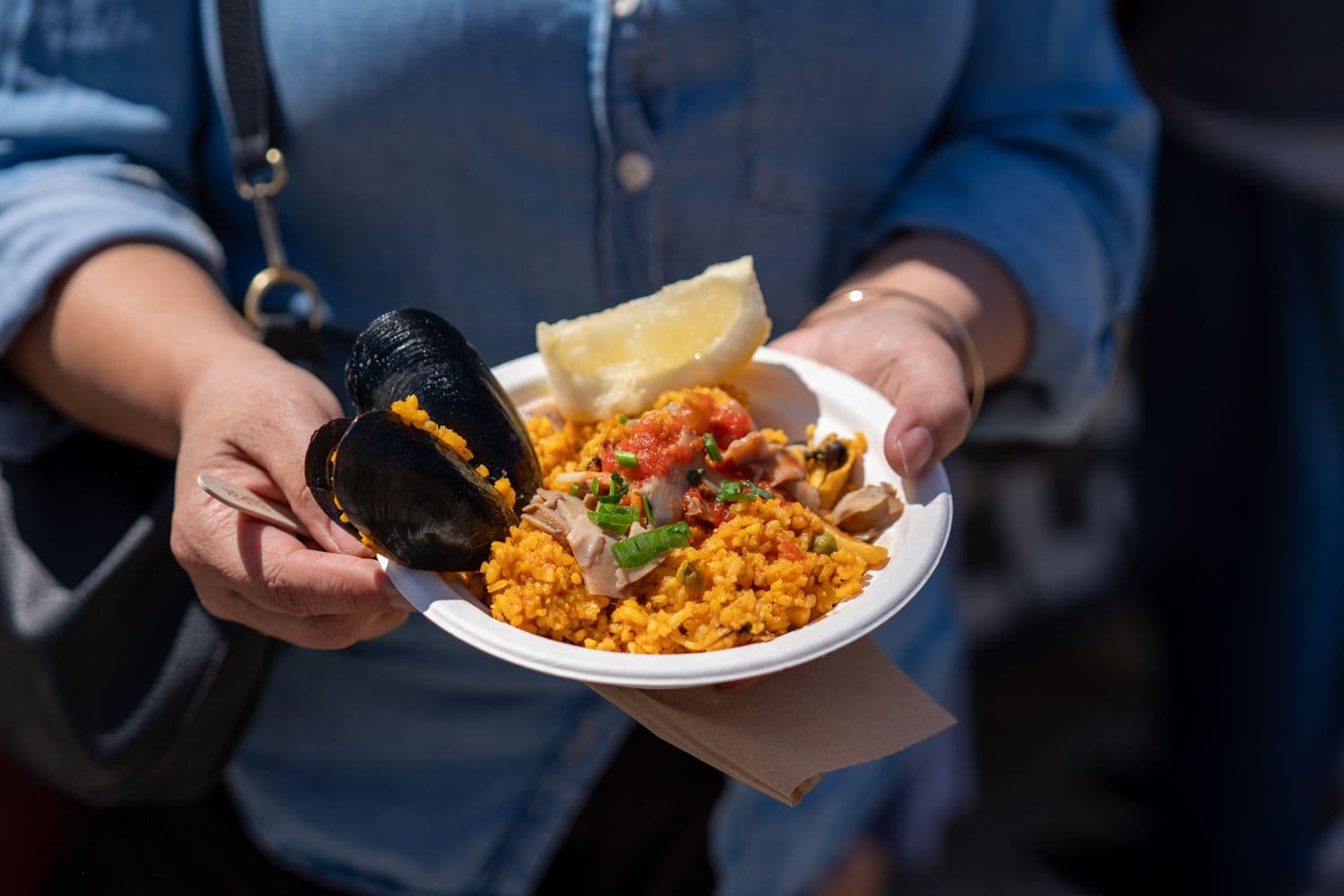 Person holding plate of seafood risotto with mussel and lemon wedge
