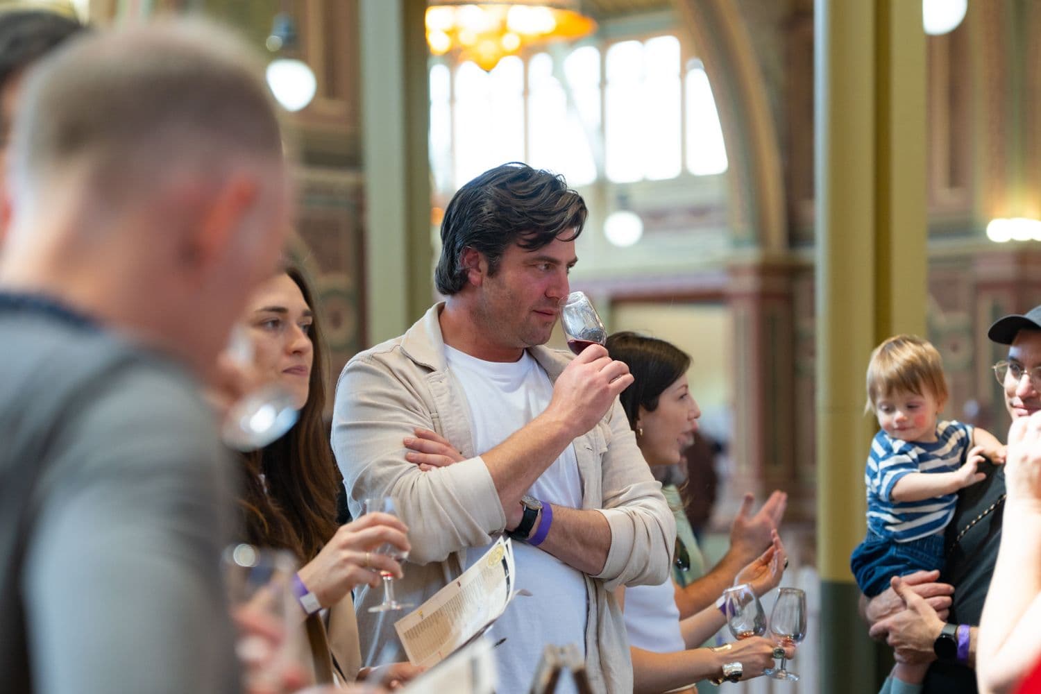 Man holding wine glass speaking to crowd at indoor tasting event