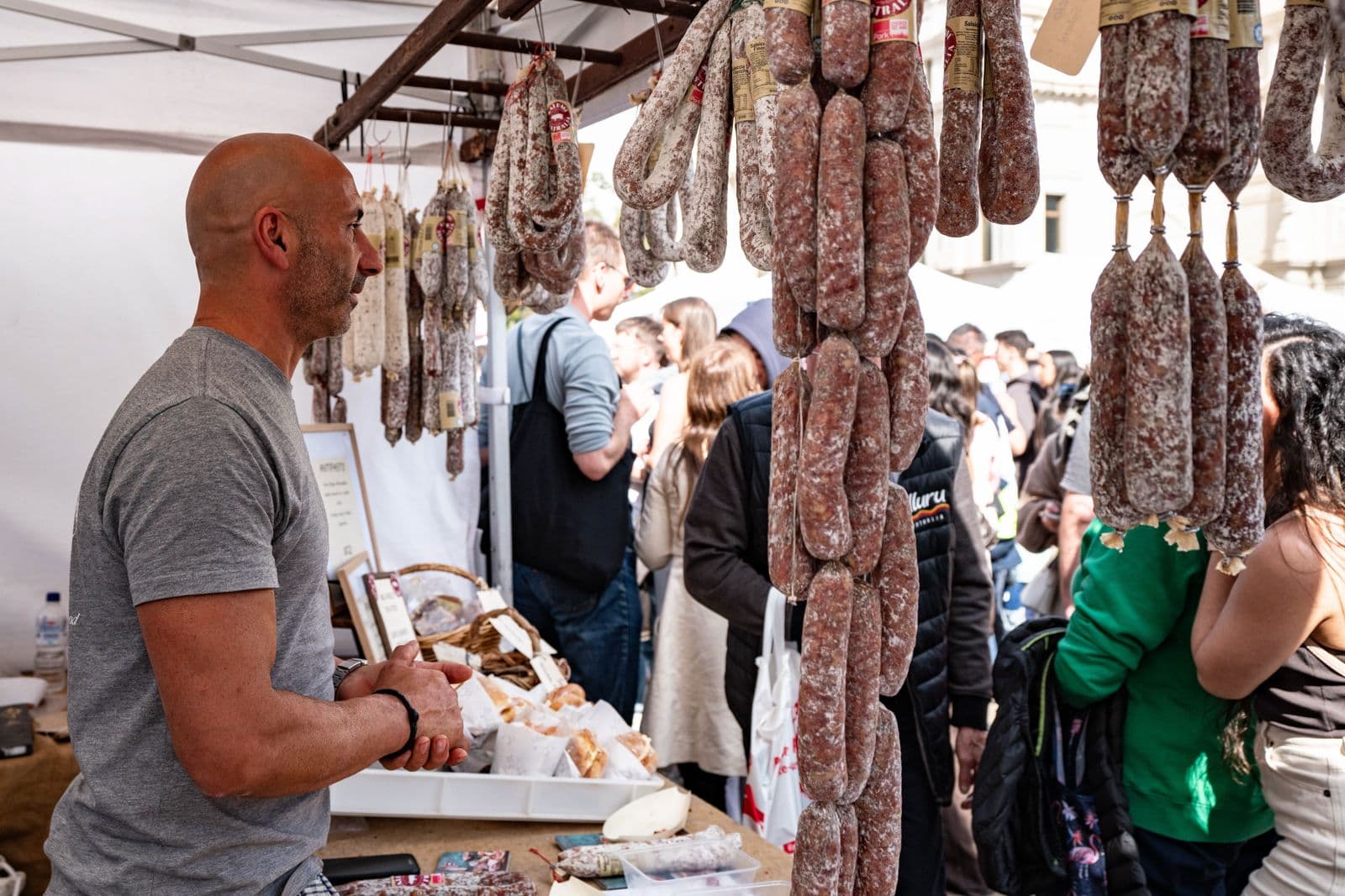Vendor at an Italian delicatessen stall with hanging cured meats
